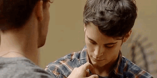 two young men are standing next to each other and one of them is adjusting the collar of the other 's shirt .