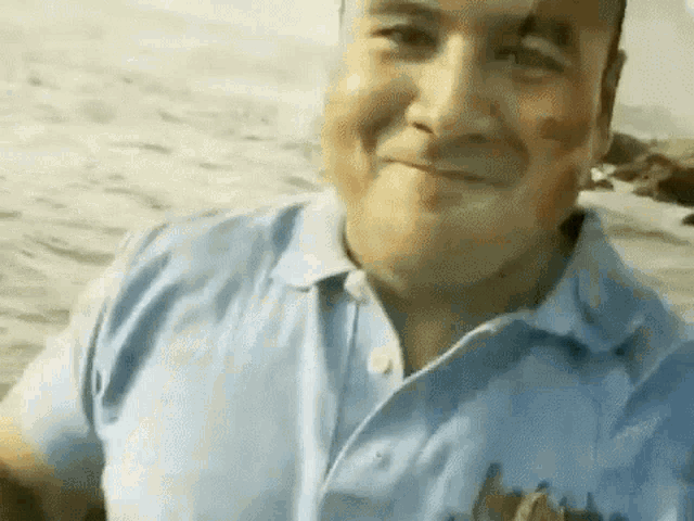 a man in a blue shirt is taking a selfie on the beach .