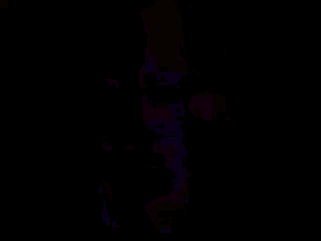 a man with glasses and a mustache is standing in front of a brick wall in a dark room .
