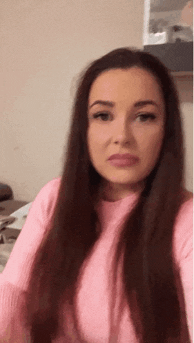 a woman with long dark hair is wearing a pink sweater and taking a selfie .