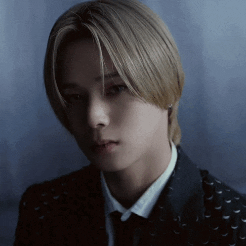a young man with blonde hair is wearing a black jacket and tie