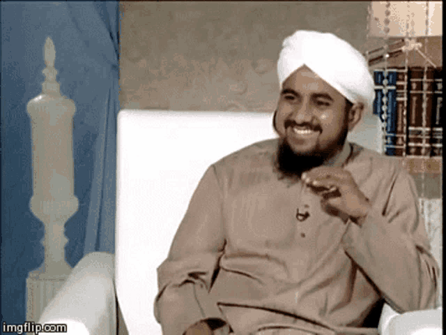 a man wearing a white turban is smiling while sitting on a chair