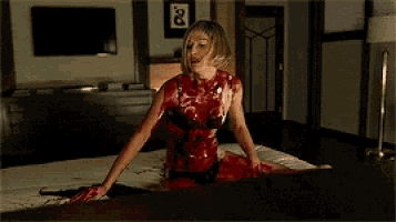 a woman covered in blood is sitting on a bed with a gun