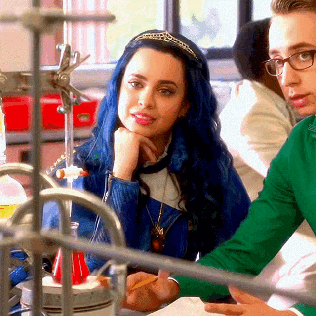 a woman with blue hair wearing a tiara is sitting next to a man in a green shirt