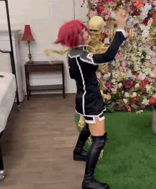 a woman with red hair is standing next to a skeleton in a room with flowers .