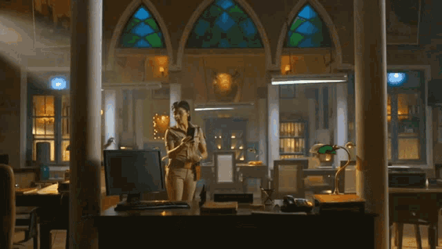 a woman stands in front of a computer in a dark room with stained glass windows