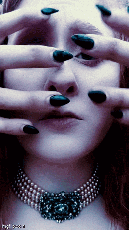 a woman with black nails and a pearl necklace is covering her eyes with her hands