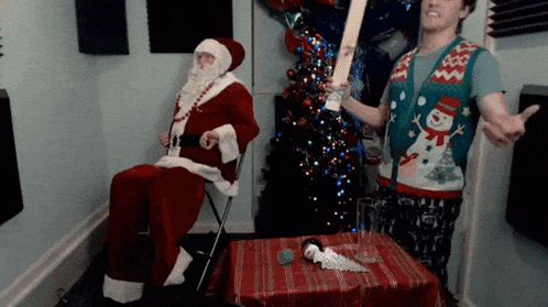 a man in a christmas sweater is standing next to a man dressed as santa claus