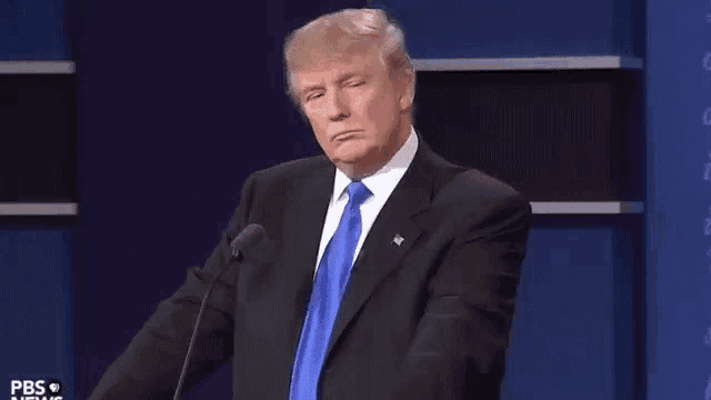 donald trump is giving a speech in front of a microphone and making a funny face .