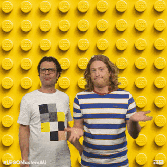 two men are standing in front of a wall made of lego bricks