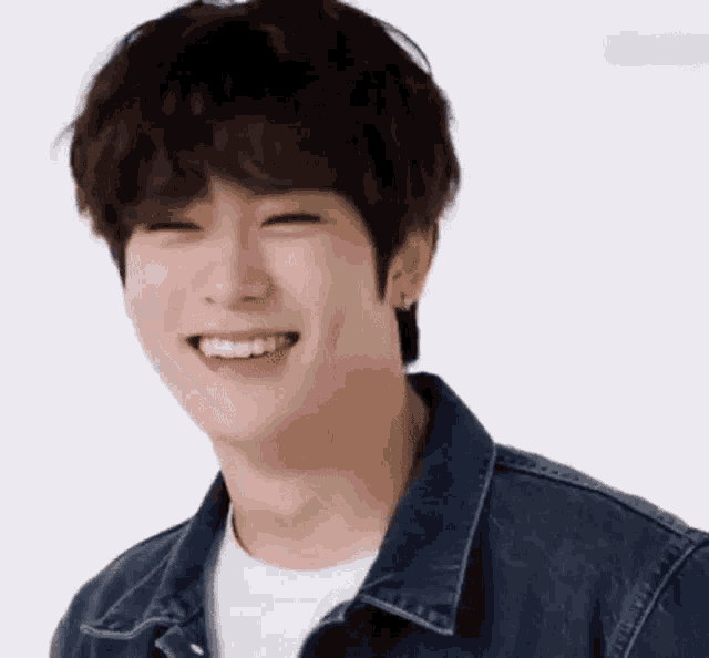 a young man wearing a denim jacket is smiling with his eyes closed .