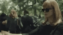a woman wearing sunglasses is standing in front of a crowd of people holding a gun .