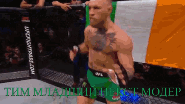 a man in a green ufc shorts is standing in a cage with a banner that says ufcfightpass.com