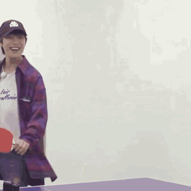 a man in a purple shirt is holding a ping pong paddle and smiling