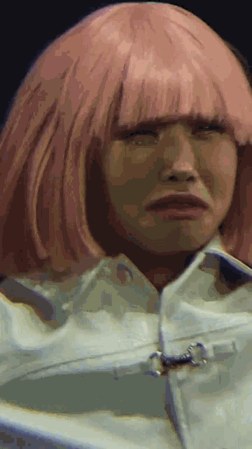 a woman wearing a pink wig and a white jacket makes a funny face