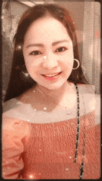 a woman wearing a pink off the shoulder top and hoop earrings smiles for the camera