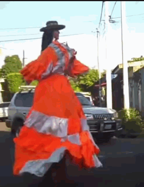 a woman wearing an orange dress and a hat is walking down the street