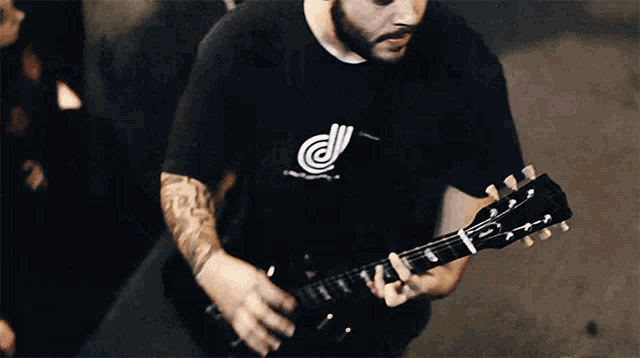a man wearing a black shirt with the letter d on it is playing a black guitar
