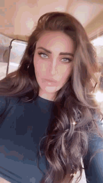a woman with long brown hair and blue eyes is taking a selfie in a car .