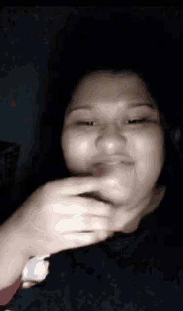 a woman is making a funny face in a dark room while wearing a watch .