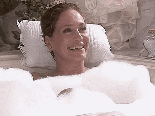 a woman is taking a bath in a tub filled with foam and smiling .