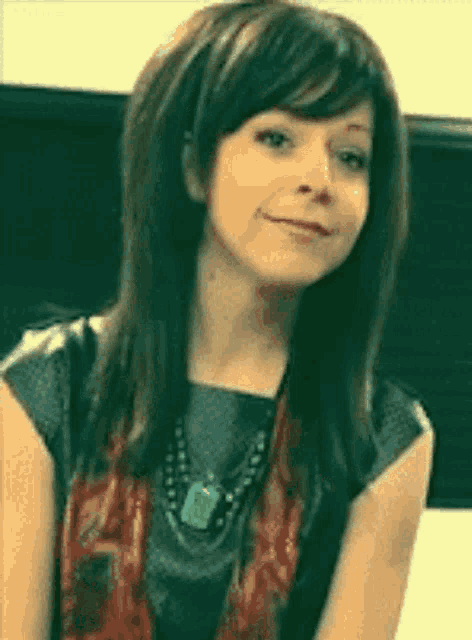 a woman wearing a scarf and a necklace smiles at the camera