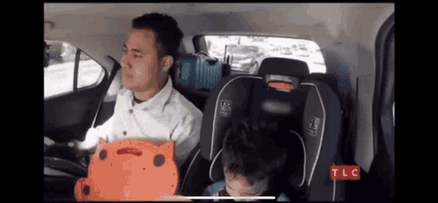 a man is driving a car while a child is sleeping in a car seat .