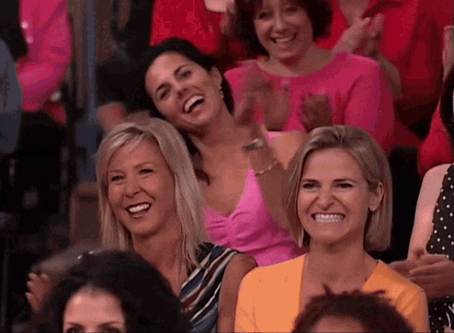 a group of women are sitting in a theatre applauding and smiling