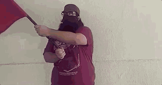a man with a beard and glasses is holding a red flag .