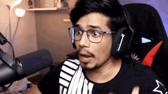 a man wearing glasses and headphones is sitting in front of a microphone and making a surprised face
