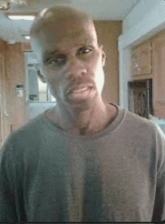a bald man in a grey shirt is standing in a kitchen .