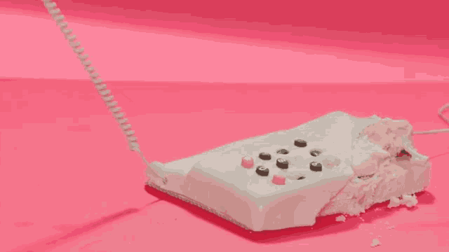 a woman 's hand is reaching for a white telephone that is covered in pink icing .