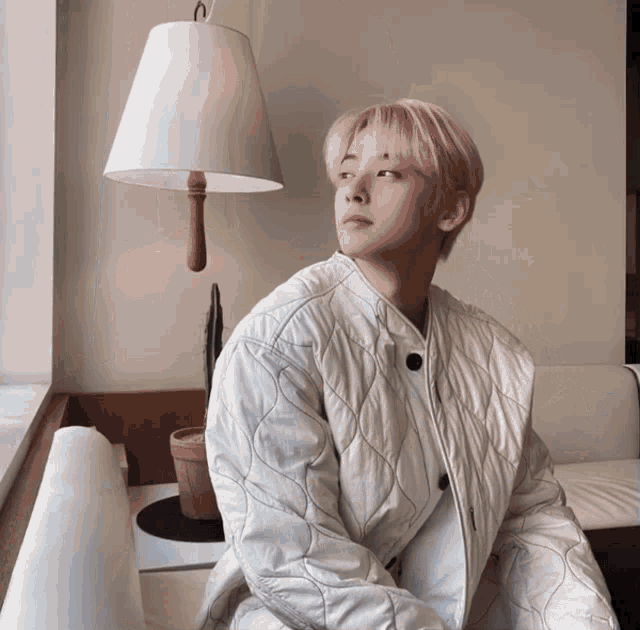 a man with pink hair is sitting in front of a white lamp