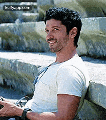 a man is sitting on a bench and smiling while looking at his phone .
