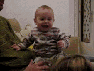 a baby is laughing while sitting on a couch with his parents .
