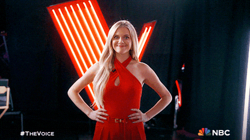 a woman in a red dress stands with her hands on her hips in front of a neon sign that says nbc