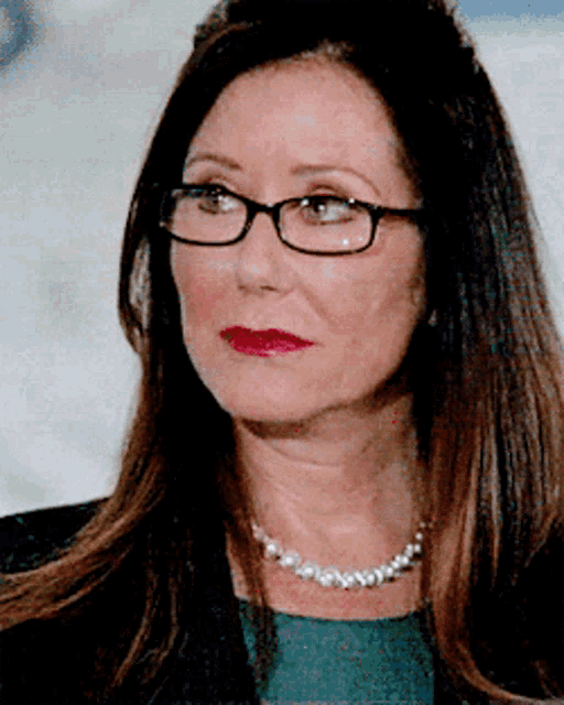 a woman wearing glasses and a pearl necklace looks serious