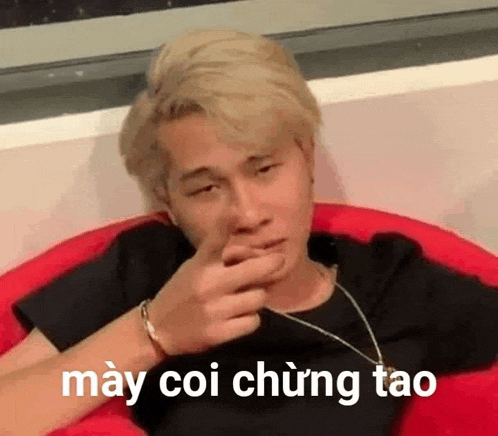 a young man is sitting in a red chair and making a funny face with his hand .