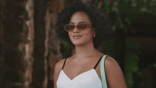 a woman wearing sunglasses and a white top is smiling