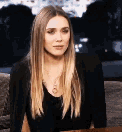 a woman wearing a black jacket and a gold necklace looks at the camera