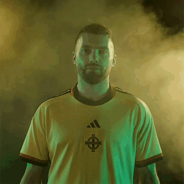 a man wearing a yellow adidas shirt with a celtic cross on it