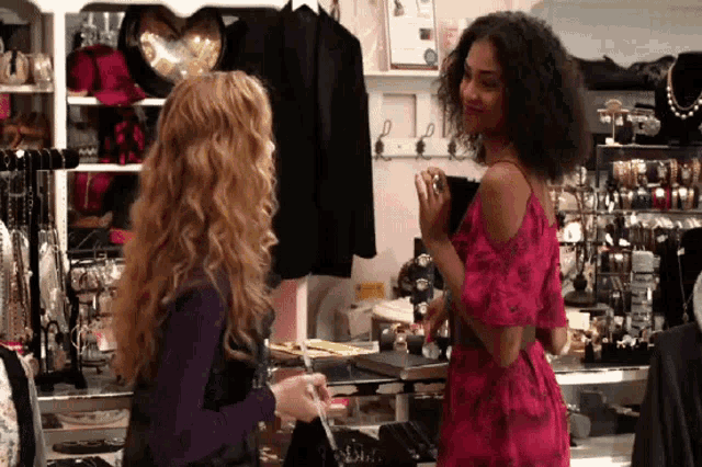 a woman in a pink dress talks to another woman in a jewelry store