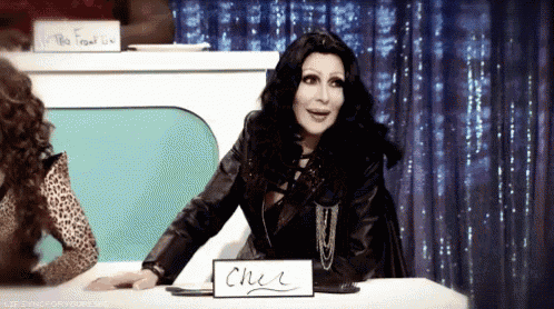 cher is sitting at a table with a sign that says cher
