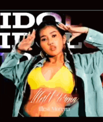a woman wearing a yellow bra and a blue jacket is dancing in front of a sign that says idol