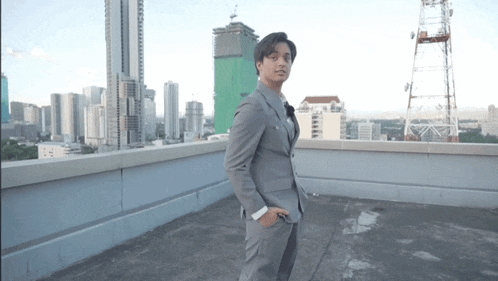 a man in a suit is standing on a rooftop with a city in the background