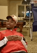 a man wearing a baseball cap and a red jacket is sitting in a chair in front of a pool table .