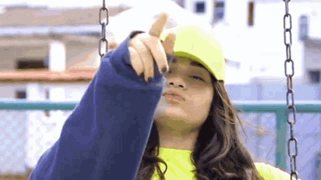 a woman wearing a yellow hat and a blue sweater is pointing at the camera