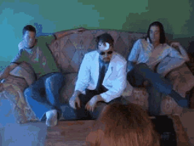 a group of people are sitting on a couch and one of them is wearing a white shirt and tie .
