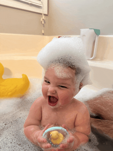 a baby is taking a bath with foam on his head and holding a rubber duck