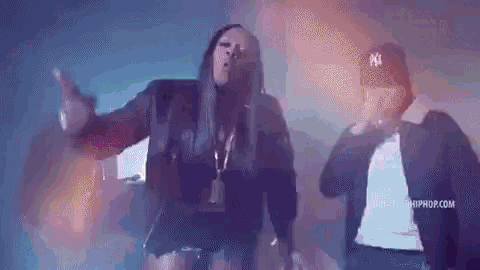 a man and a woman are dancing together in a dark room . the woman is wearing a ny hat .